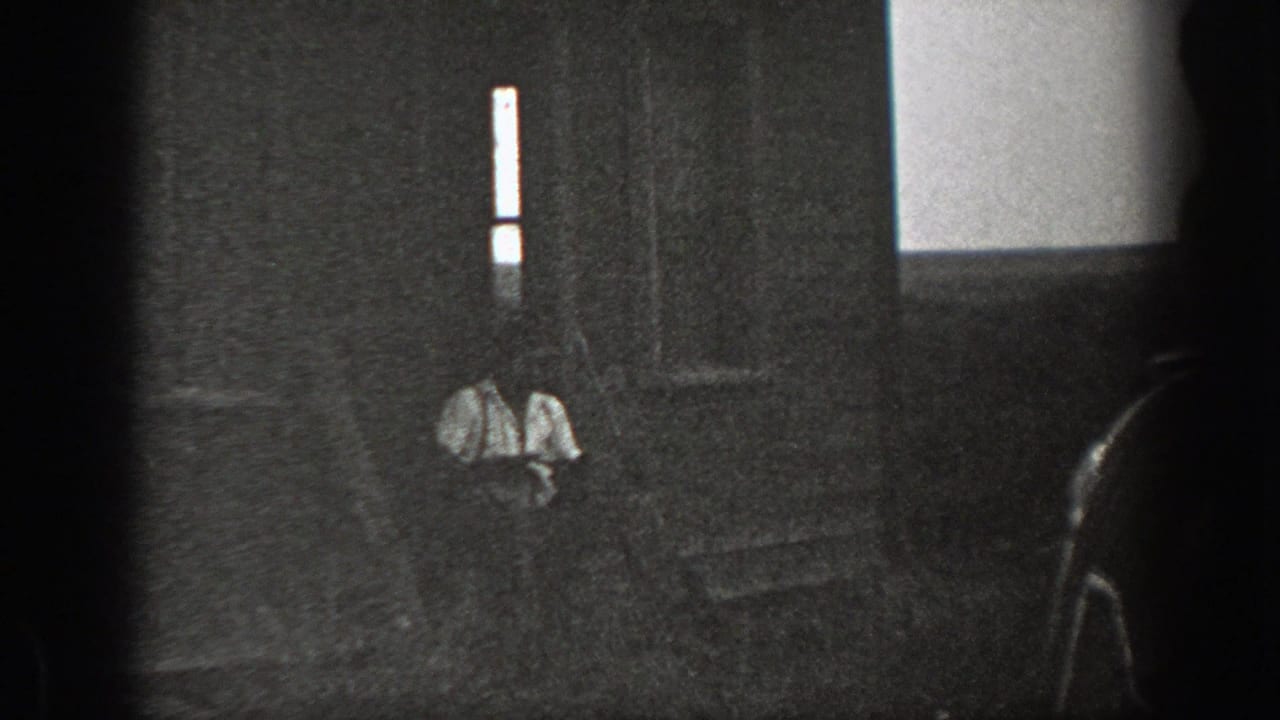 Dark black-and-white frame with men seated near a step or doorway.