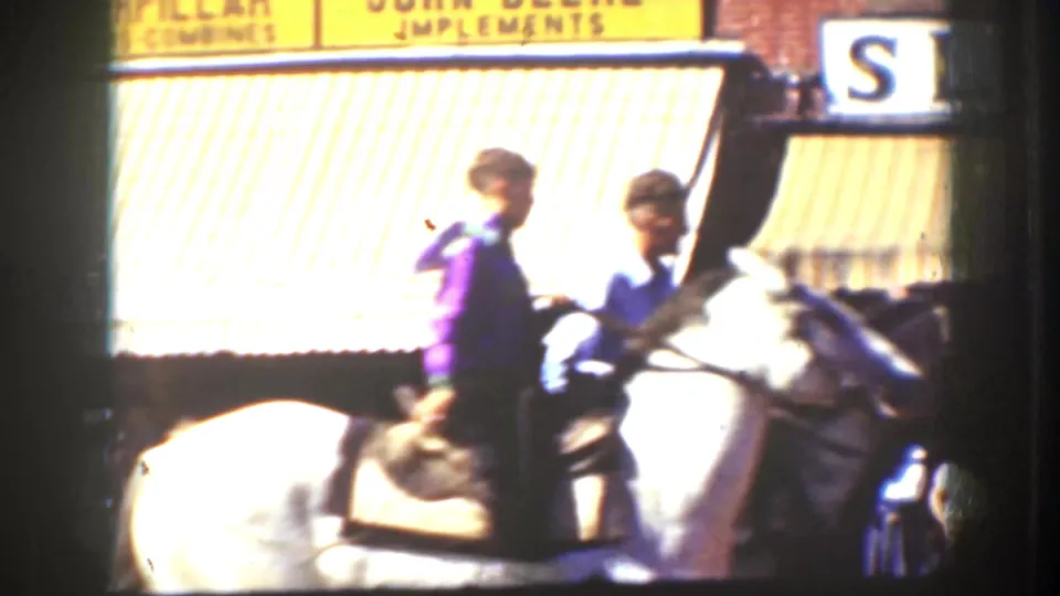 Color 8mm frame from California, 1939, with two riders on a white horse passing storefront awnings and visible signage.