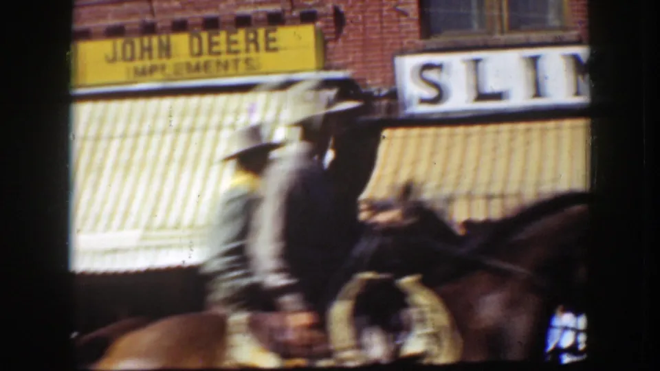 Color 8mm frame from California, 1939, with horseback riders moving past a John Deere Implements storefront sign and awning.