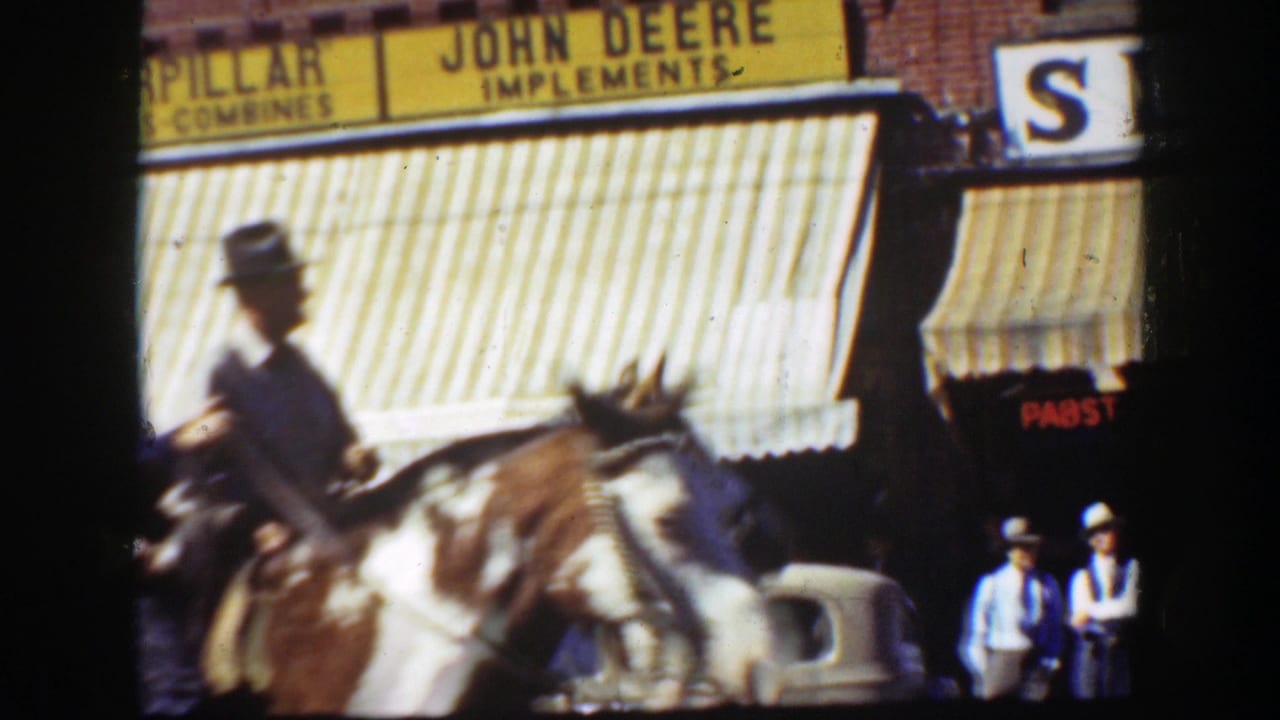 Horseback rider passes storefront awnings with John Deere signage in the background.