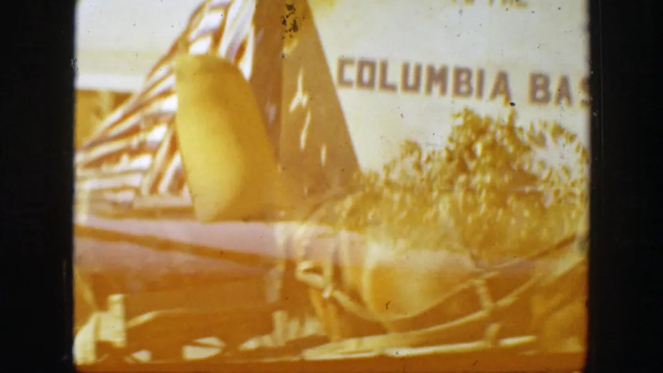 Faded 1939 California parade frame with a float element in the foreground and a partially readable Columbia Basin sign behind trees.