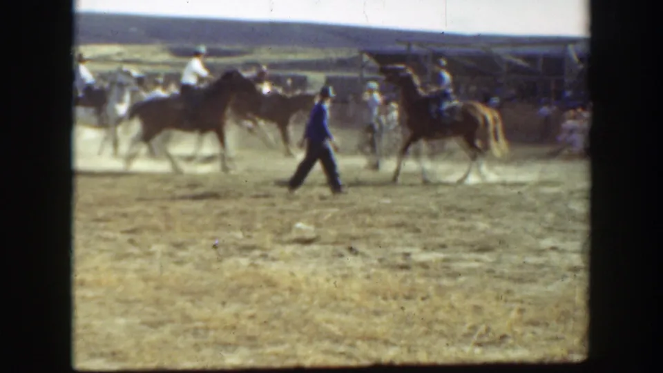 1939 California home-movie frame showing a man crossing in front of mounted riders and horses near a spectator area.