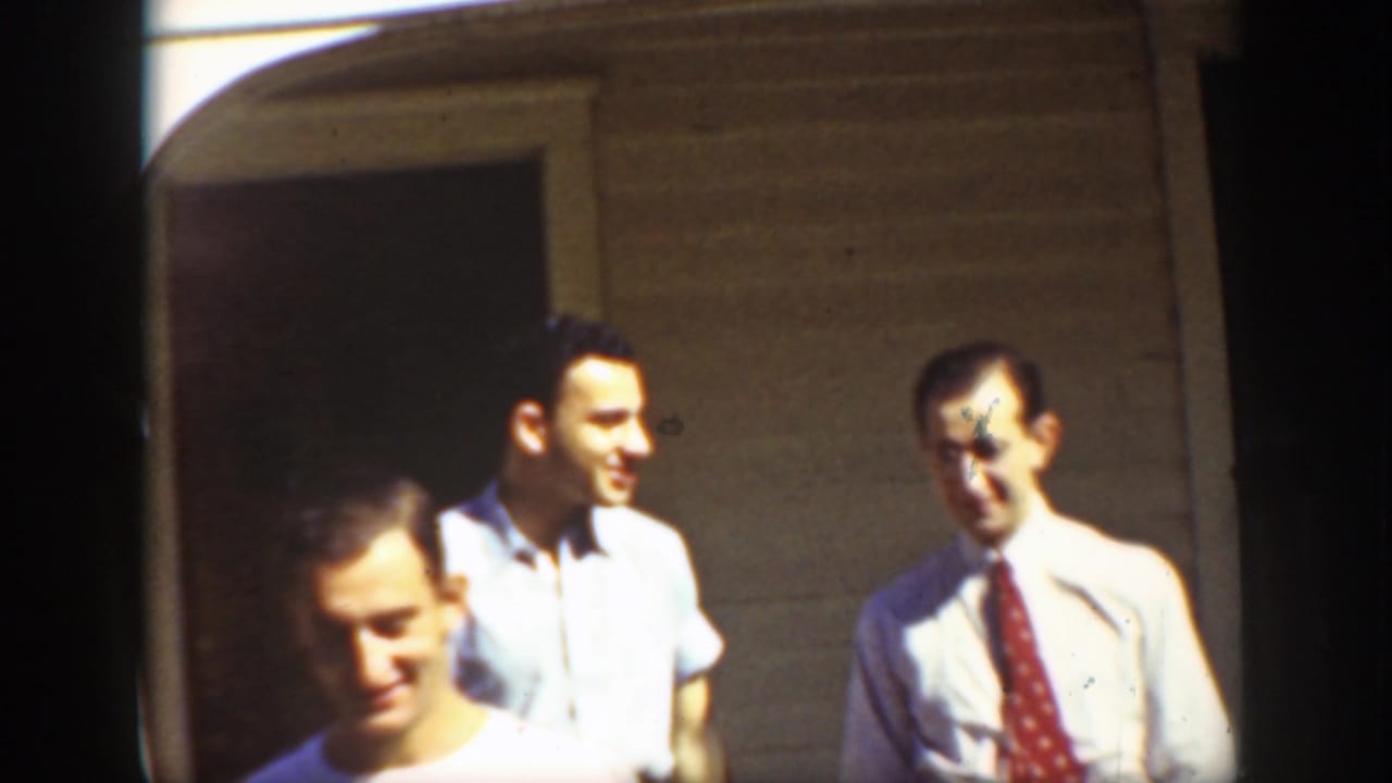 Three men standing outside a house wall in bright sunlight.
