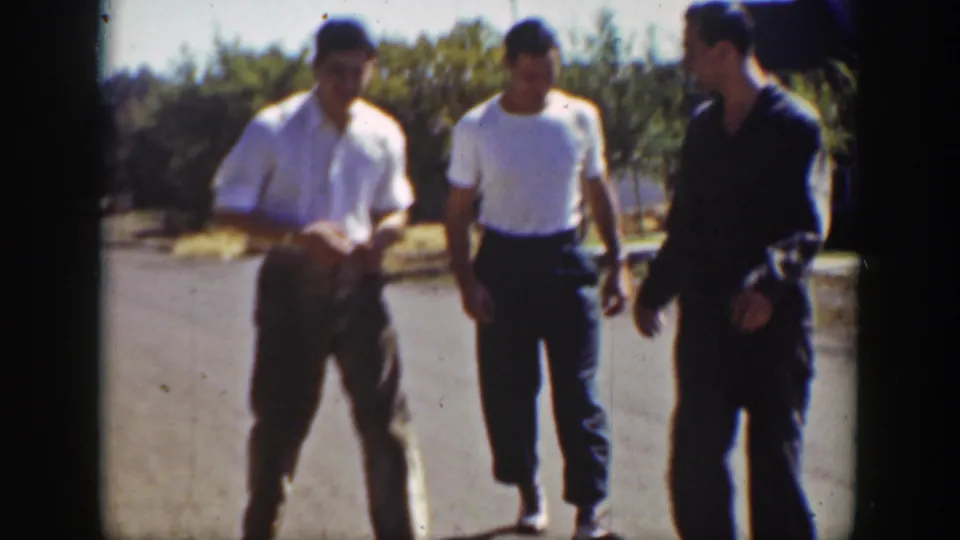 Three young men walk along a quiet California street in 1939 footage, with shrubs and open ground behind them.
