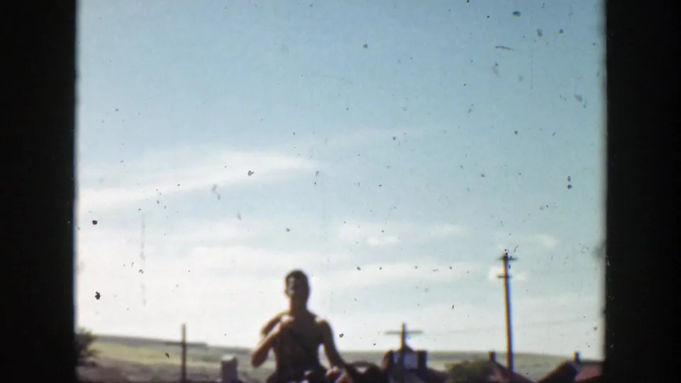 A distant horseback rider appears under a pale sky in 1939 California home-movie footage, with roadside poles and open land.