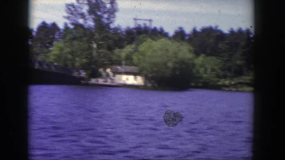 1953 Wisconsin 8mm frame looking across rippled water toward trees and shoreline, with part of the bridge at the left edge.