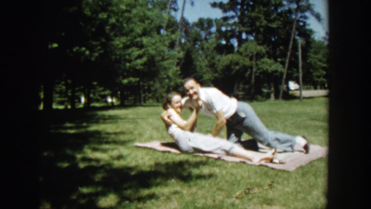 Man leans over woman on a picnic blanket in a grassy park.