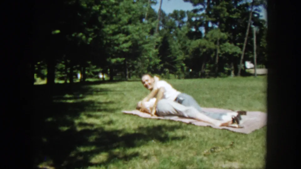 The man and woman recline together on a blanket in a tree-lined Wisconsin park, filmed on 8mm in 1953.