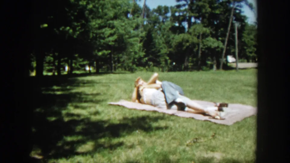The couple remains in a close embrace on a blanket in the Wisconsin park, with trees and sunlit grass behind them.