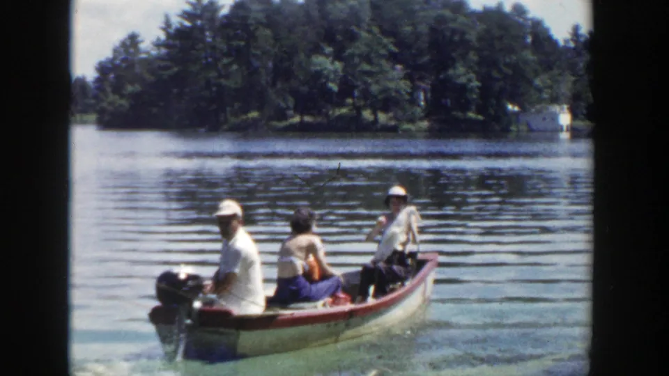 The Wisconsin lake scene shows three adults seated in a small motorboat as the driver looks back toward the camera.