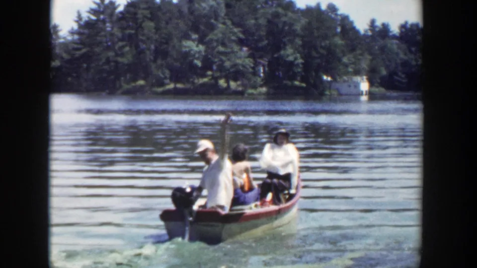Three adults in a small motorboat move away on a Wisconsin lake, with one person lifting an arm near the stern.