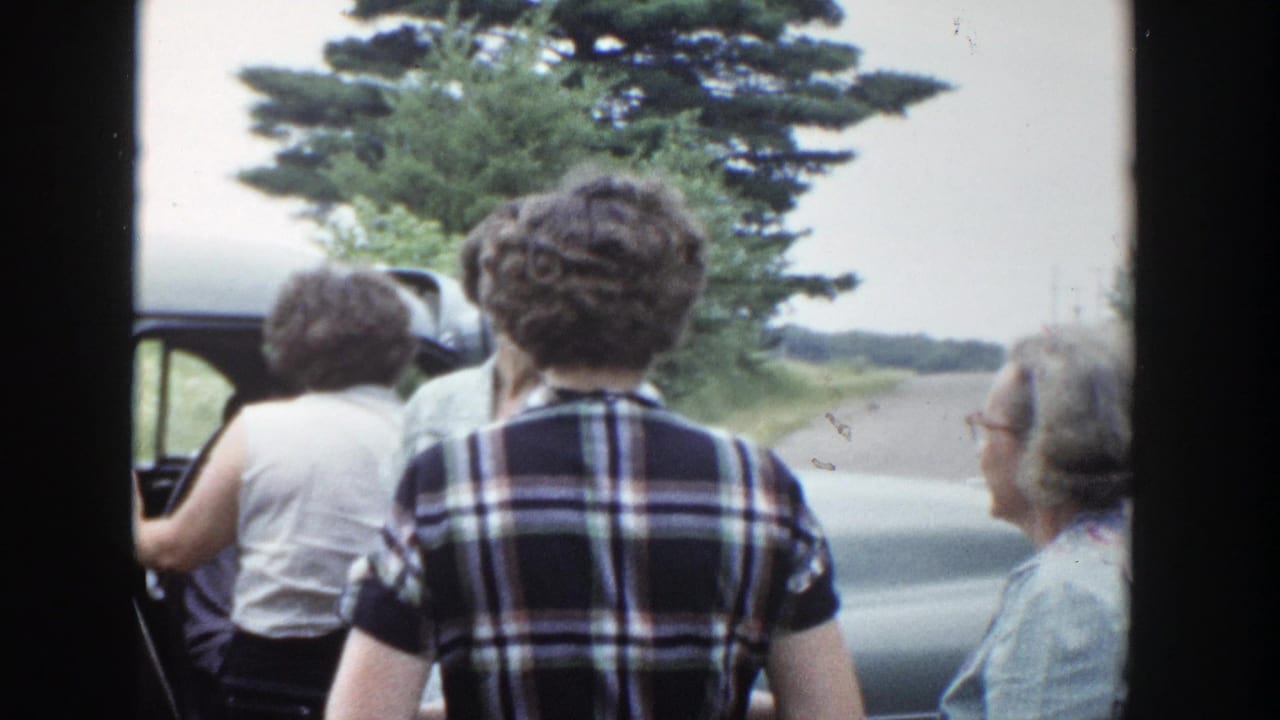 Women gather beside a mid-century car in rural Wisconsin, filmed from a handheld home-movie viewpoint.