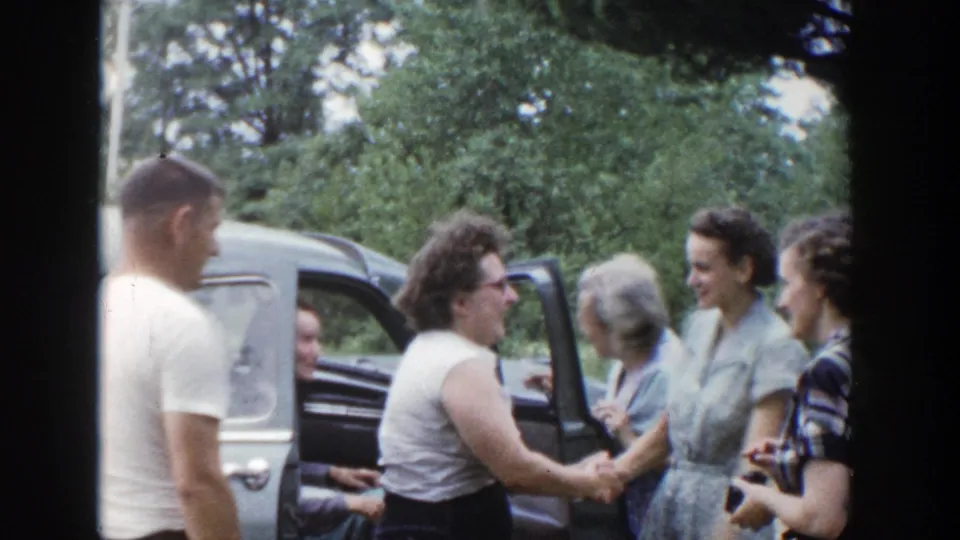 Adults in 1950s clothing smile and shake hands beside an open car door in Wisconsin home-movie footage.