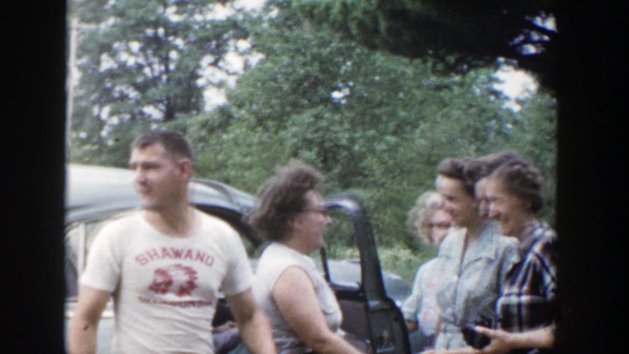 Four adults laughing beside a parked car with trees behind them.