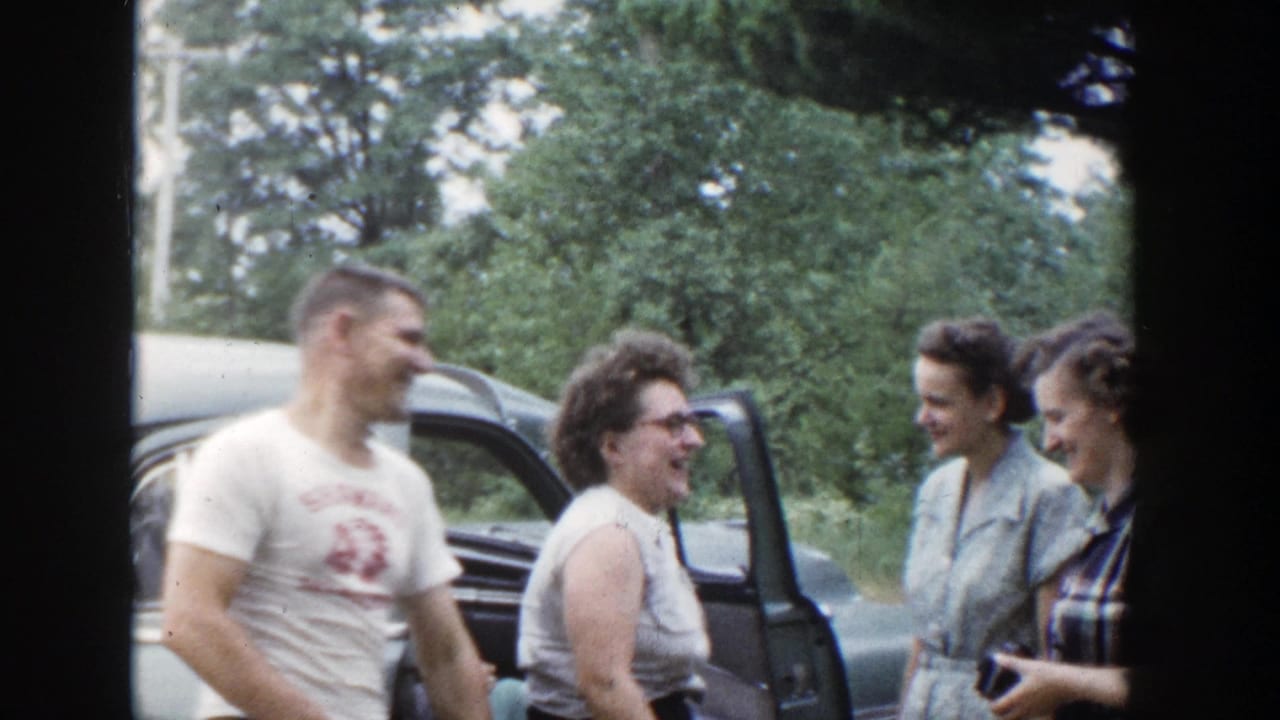 Man and three women smiling near an open car door outdoors.