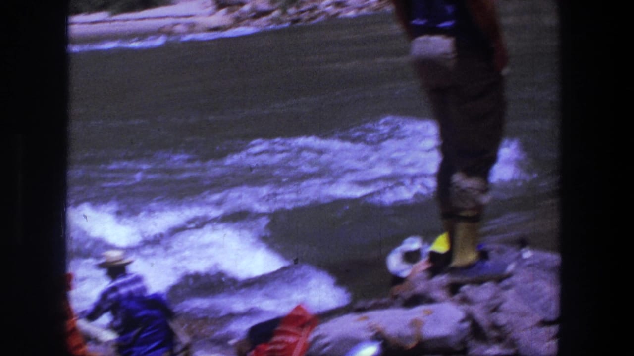 1969 Utah 8mm frame showing people near a fast river, including a man standing on rocks and others seated nearby.