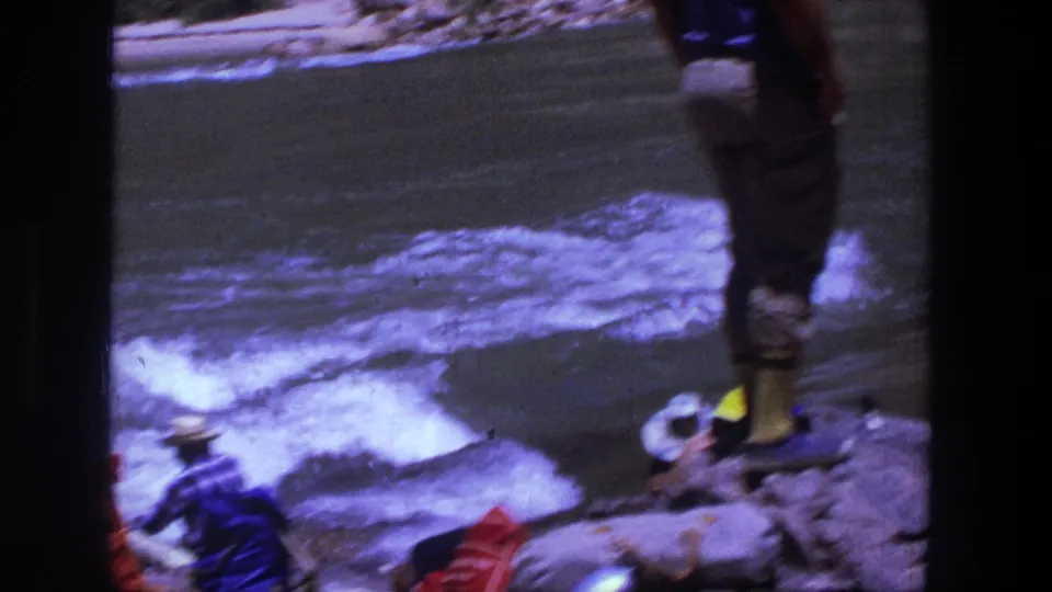 1969 Utah 8mm frame showing people near a fast river, including a man standing on rocks and others seated nearby.