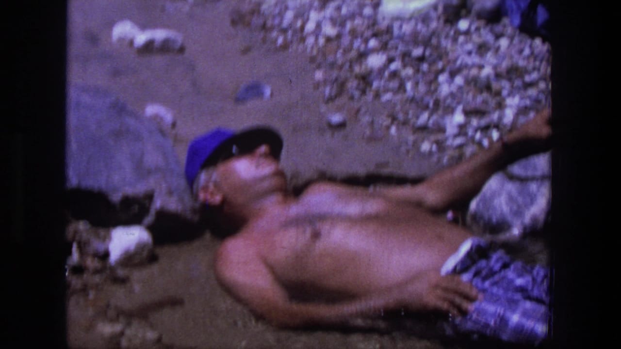 Man in blue cap reclines on rocks with one arm extended near the shoreline.