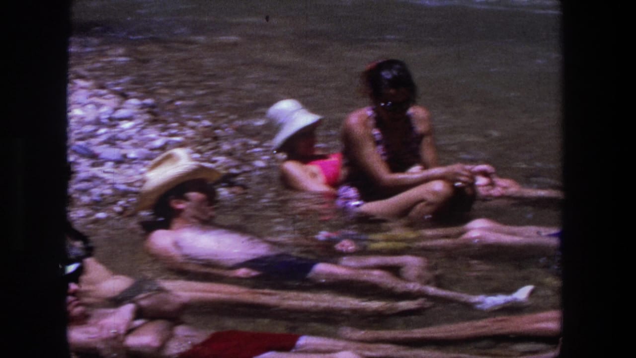 Group of adults relax in shallow water, with one person sitting upright near others reclining.
