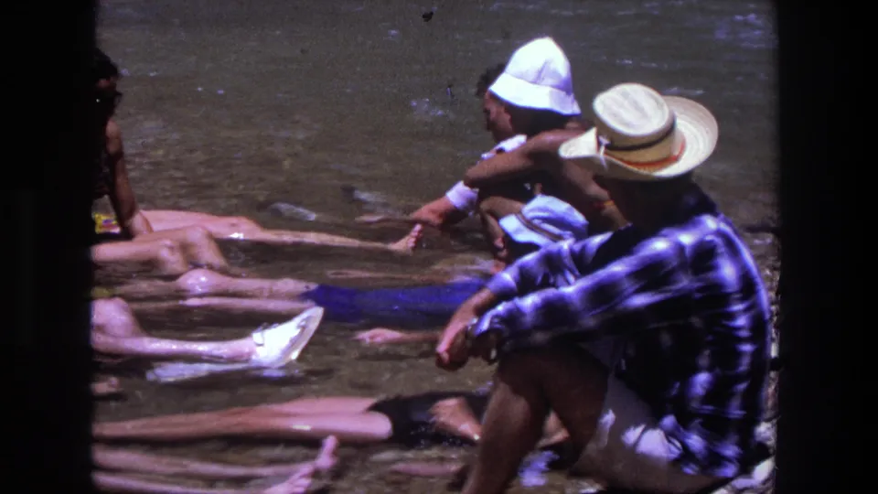 1969 Utah river scene with adults in swimsuits and hats resting in shallow water, including a nearby man in a plaid shirt.