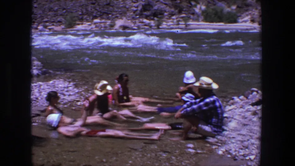1969 Utah footage shows adults in swimwear and sun hats resting in a shallow river channel.