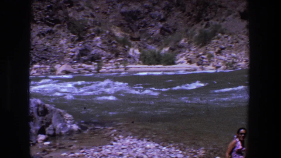 Utah canyon river rapids fill the frame while a person is partly visible near the right edge in the 1969 home-movie scene.