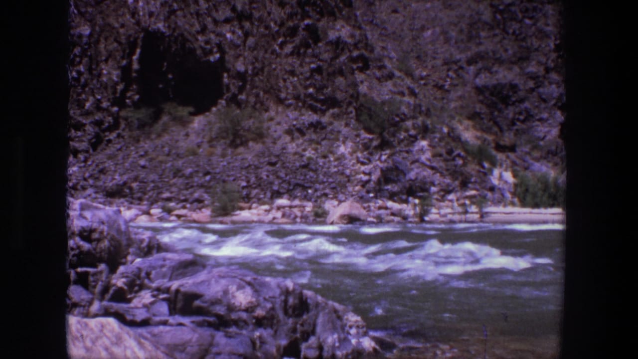 1969 Utah 8mm frame showing fast river water, rocks, and a rugged canyon bank from a home-movie viewpoint.