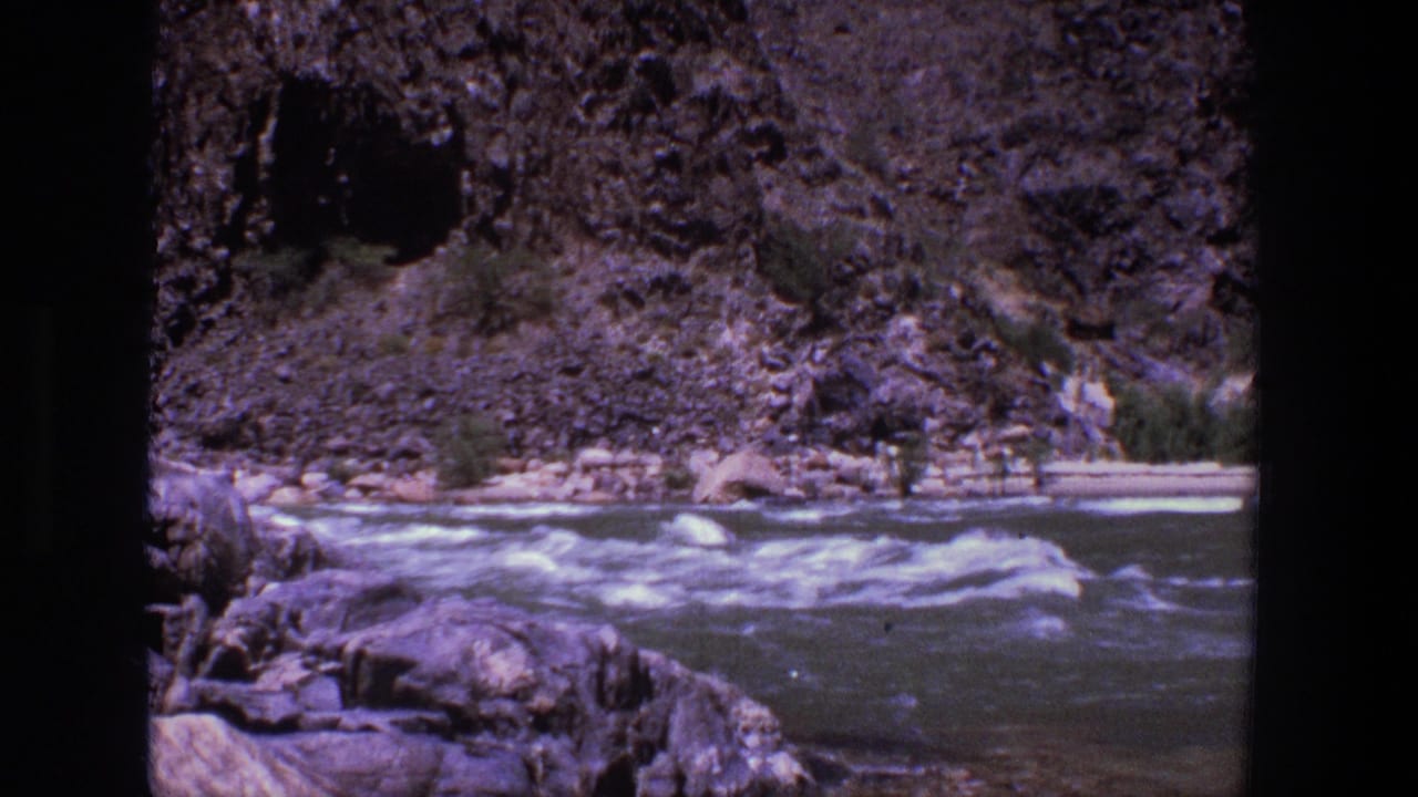 Whitewater river flowing past rocks and a steep canyon bank.