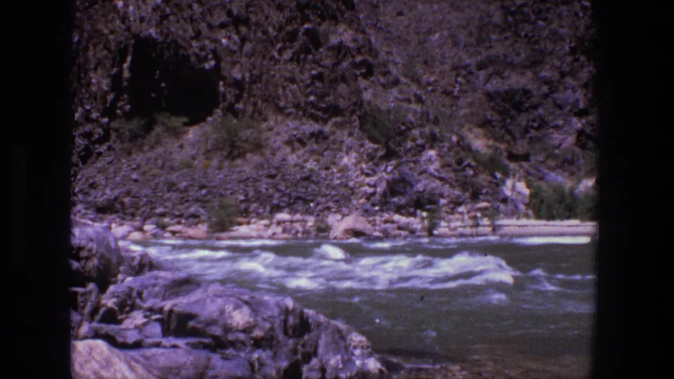 1969 Utah home-movie view of river rapids beside a rocky bank and steep, shadowed canyon wall.