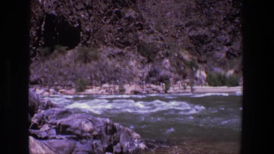 Utah 1969 8mm frame of choppy river water, shoreline rocks, and sparse vegetation along a canyon edge.