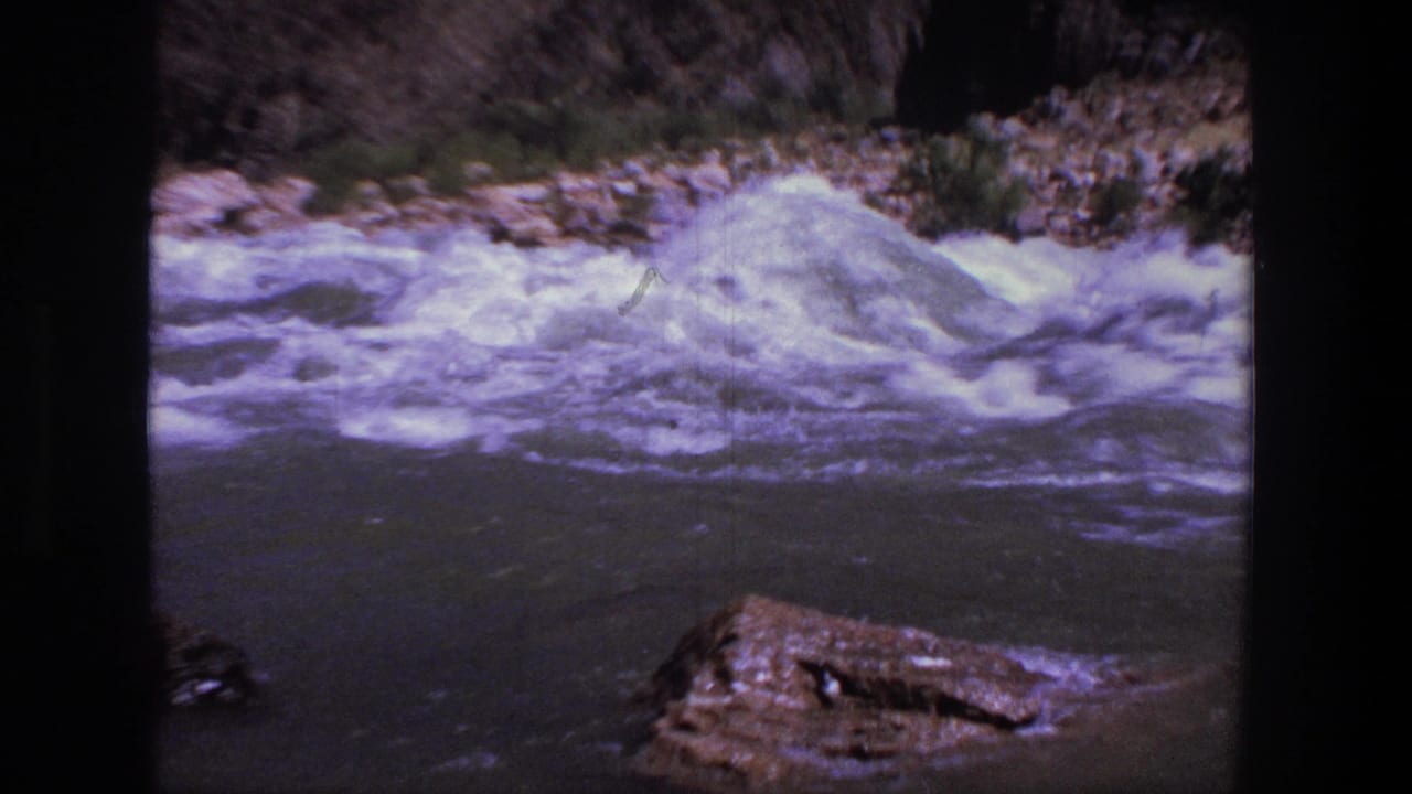 1969 Utah 8mm frame with foaming rapids moving along a rocky bank beneath a dry canyon slope.