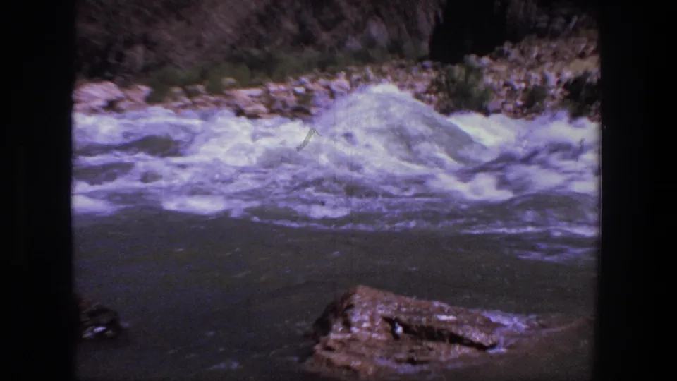 1969 Utah 8mm frame with foaming rapids moving along a rocky bank beneath a dry canyon slope.