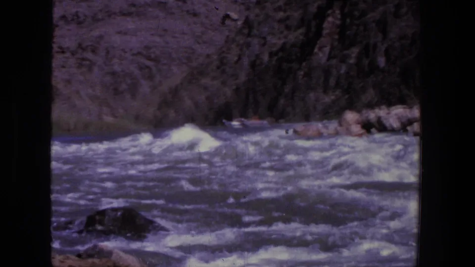 1969 Utah 8mm frame showing rapids below a steep canyon wall, with rocks breaking the water surface.