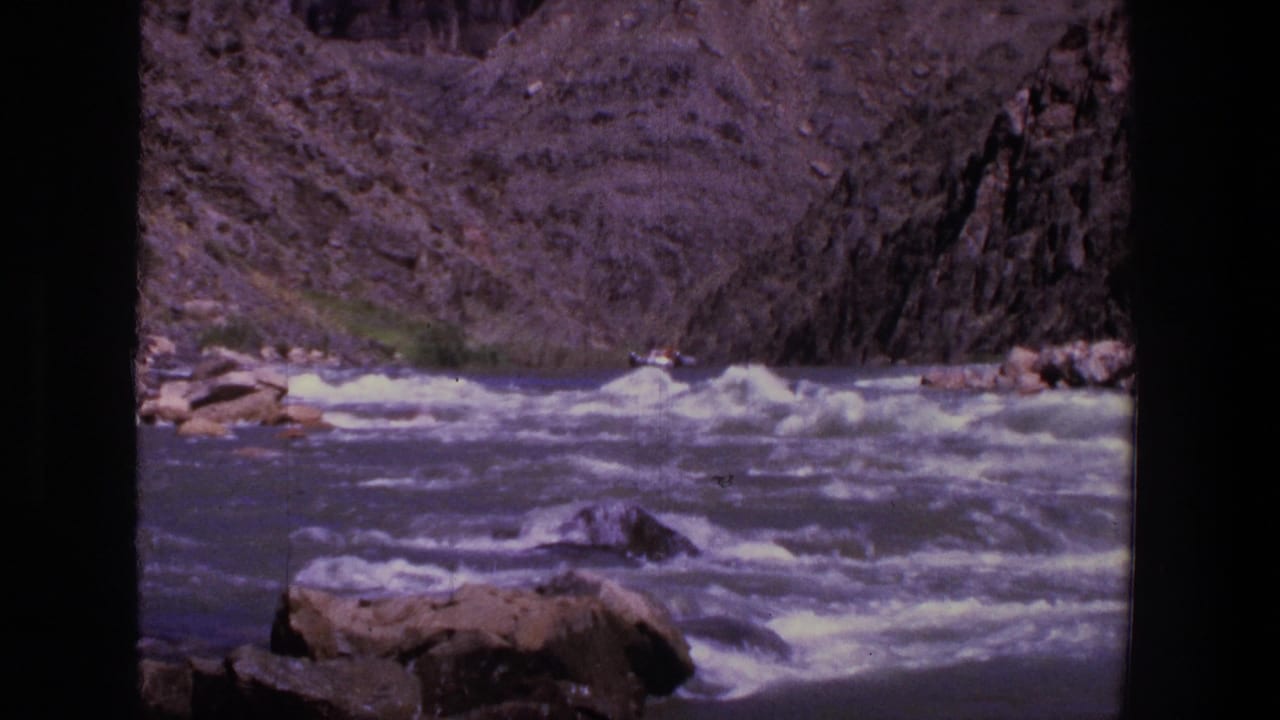 White-water rapids flowing through a rocky canyon with a small raft in the distance.