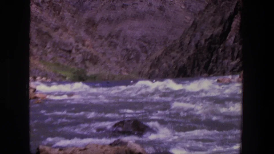 1969 Utah home-movie frame with the raft barely visible near the rapids and canyon rock in soft focus.