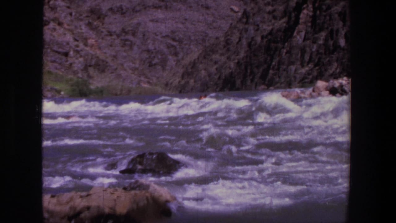 Choppy river water fills the foreground with rocks and canyon walls behind it.