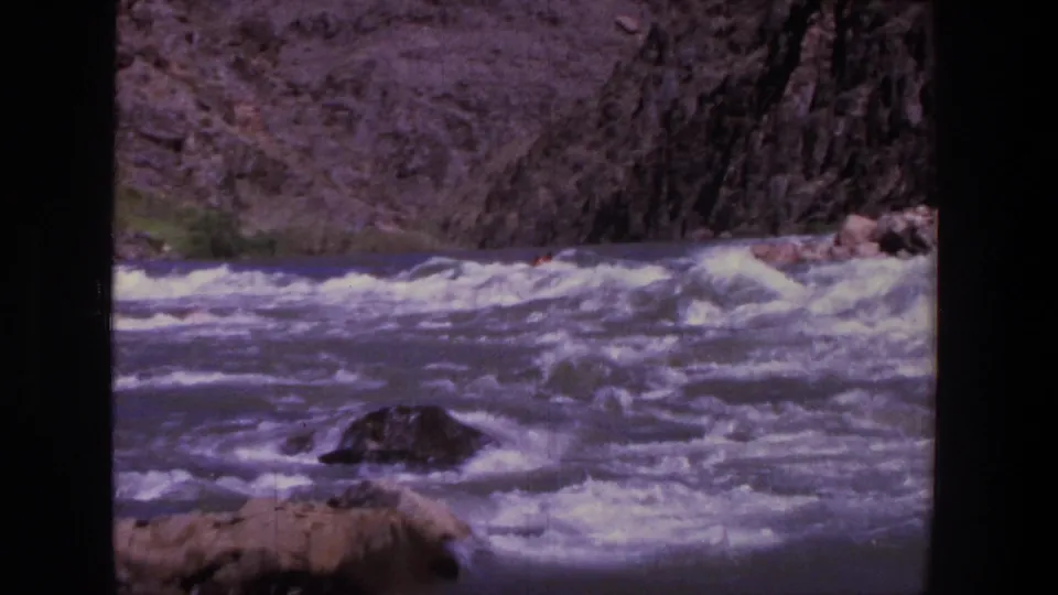 1969 Utah 8mm frame of turbulent whitewater and canyon rock, with any rafters mostly obscured by distance and waves.