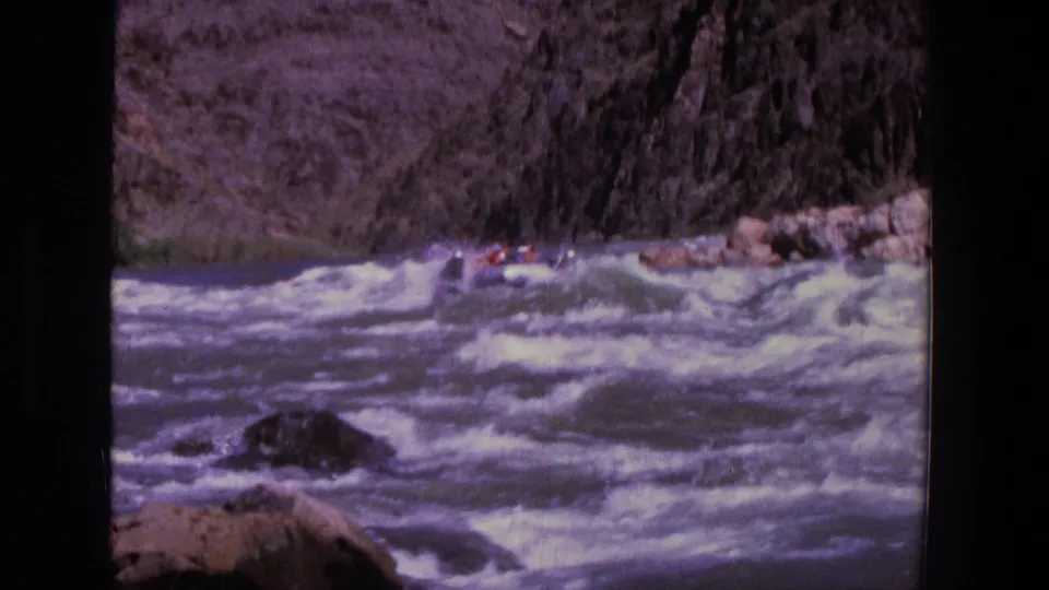 1969 Utah 8mm frame showing a small raft carrying several distant people through turbulent canyon rapids.