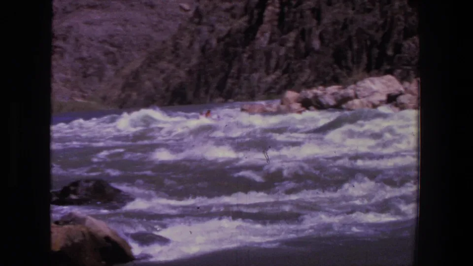 1969 Utah 8mm frame of a rocky canyon river as distant rafters continue through choppy whitewater.