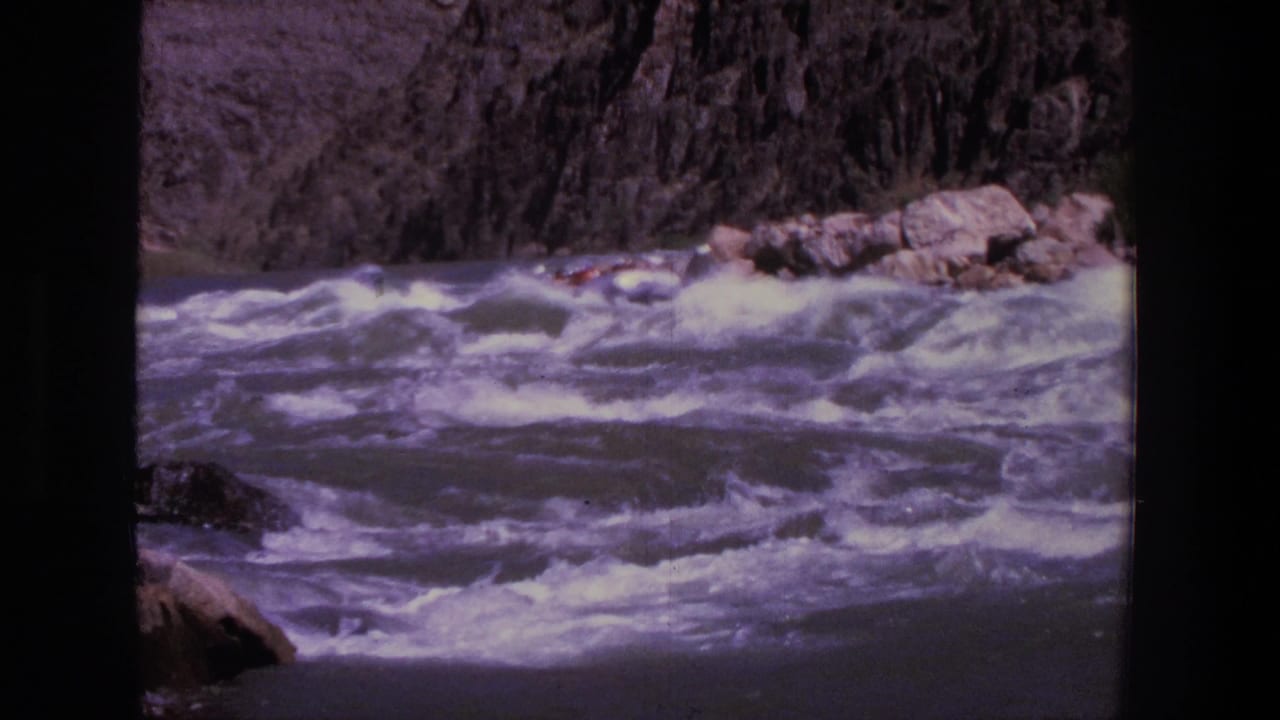 Distant raft entering whitewater rapids between rocky canyon walls.