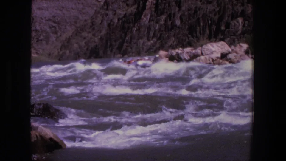 1969 Utah 8mm frame showing a distant inflatable raft moving through rough whitewater below steep rock walls.