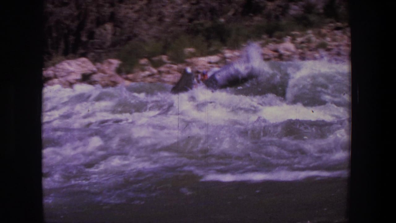 Whitewater rapids beside rocky riverbank with part of a raft just entering the frame.
