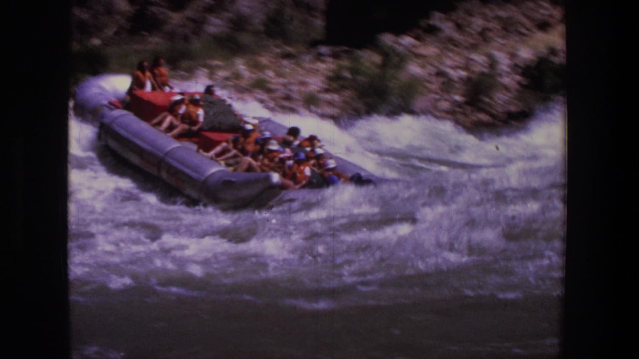 1969 Utah 8mm frame of several rafters in a silver inflatable boat riding through turbulent whitewater.