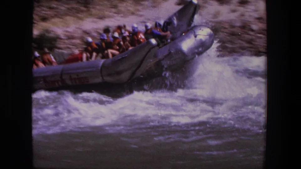 1969 Utah 8mm frame showing rafters crowded in a silver inflatable boat as it rises through splashing rapids.