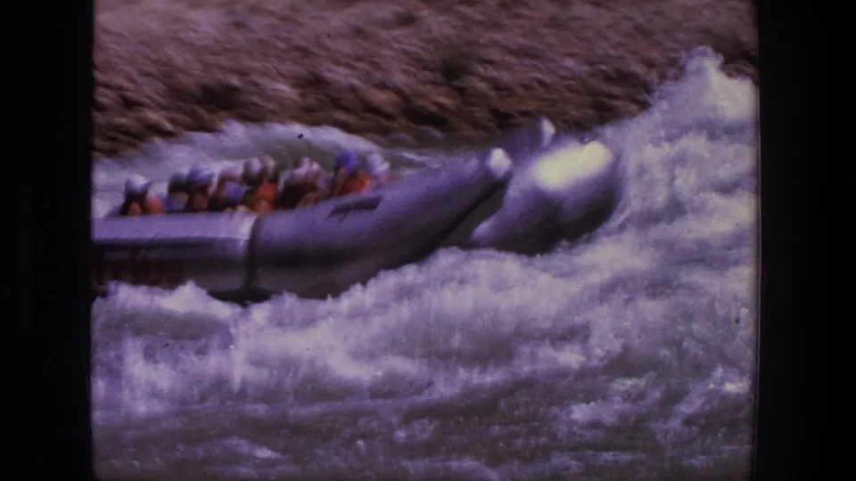 1969 Utah 8mm frame of a silver raft pushing into heavy whitewater, with rafters partly hidden by spray.