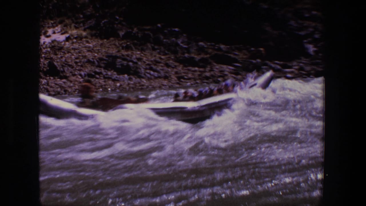 Inflatable raft moves through rough whitewater in Utah, with passengers indistinct and a rocky shoreline behind it.