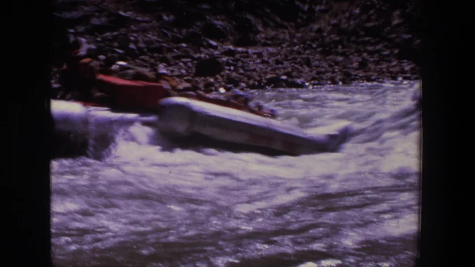 A red and white inflatable raft passes through whitewater in a 1969 Utah home movie, with people visible but indistinct.