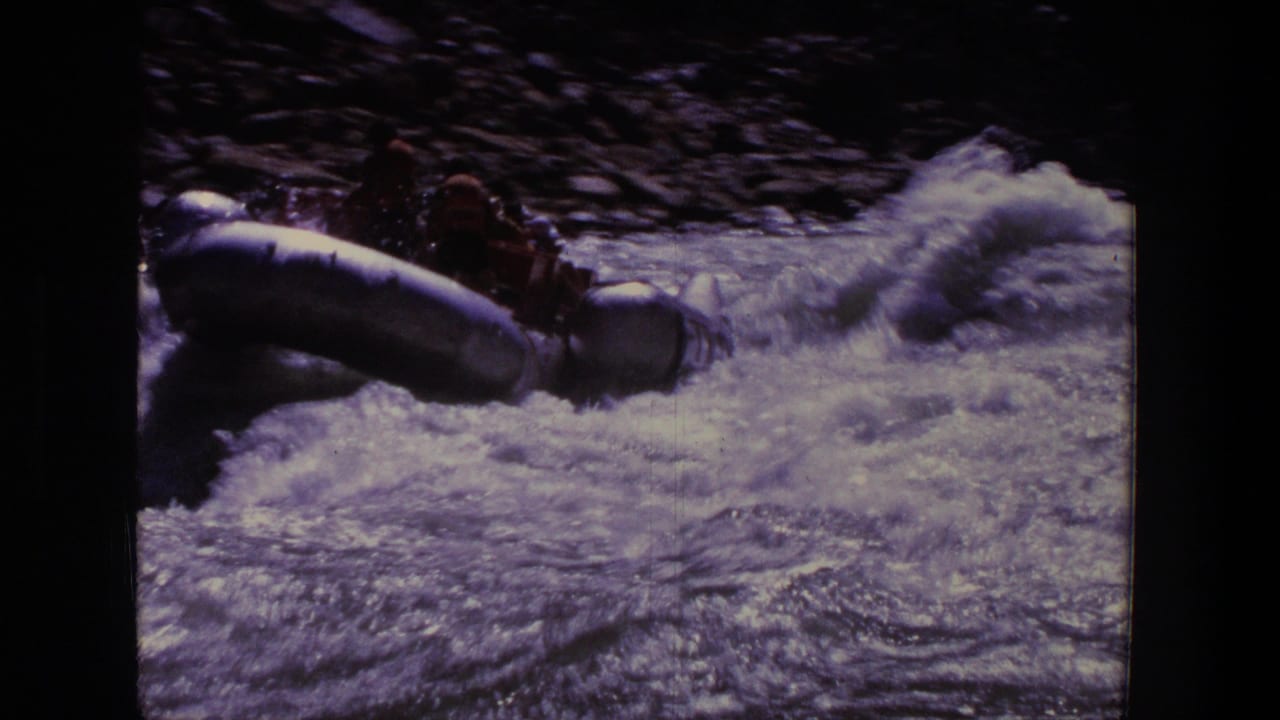 Rubber raft entering rough whitewater with passengers partly visible in shadow.