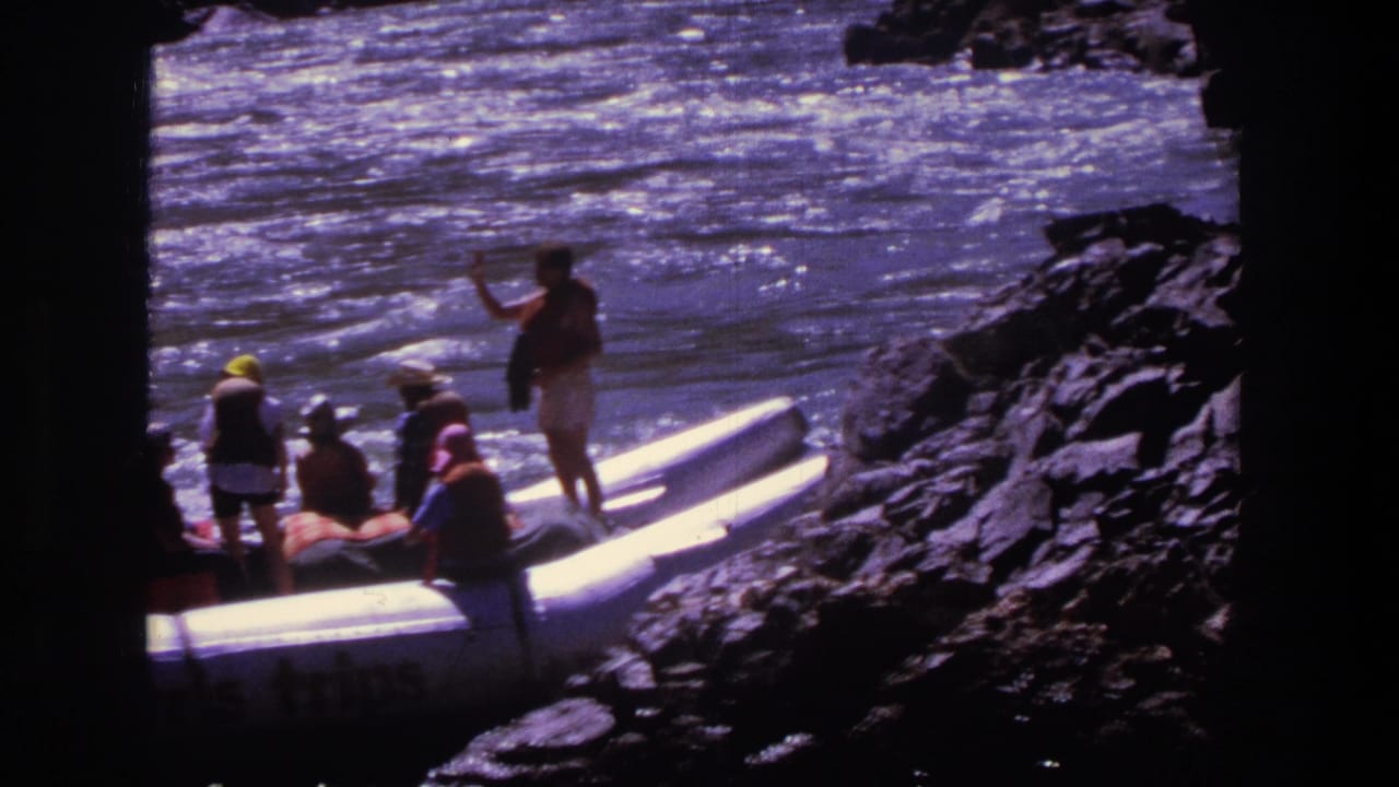 People beside white inflatable rafts near a rocky river shore.
