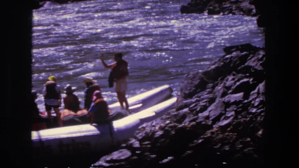 1969 Utah home-movie frame showing people near white inflatable rafts at a rocky riverbank.